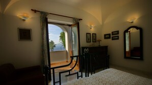 A bedroom with a large window, a bed, a dresser, and a mirror.