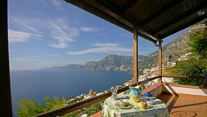A terrace with a table set for tea, overlooking a coastal landscape with mountains and a view of the sea.