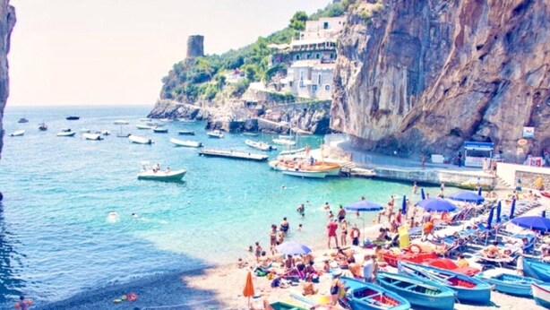 A coastal beach with boats, people, and buildings on a cliff.