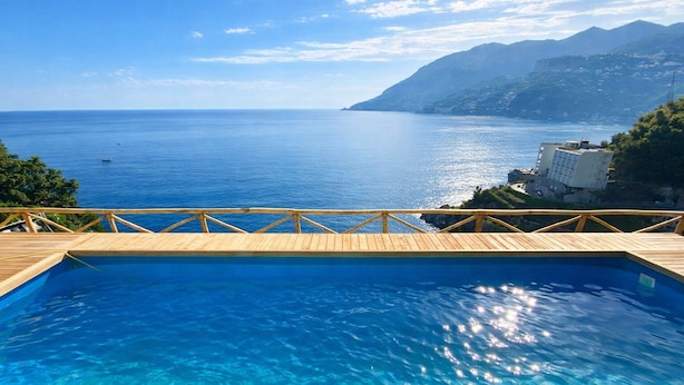 Eine Holzterrasse mit Pool mit Blick auf das Meer und Berge.