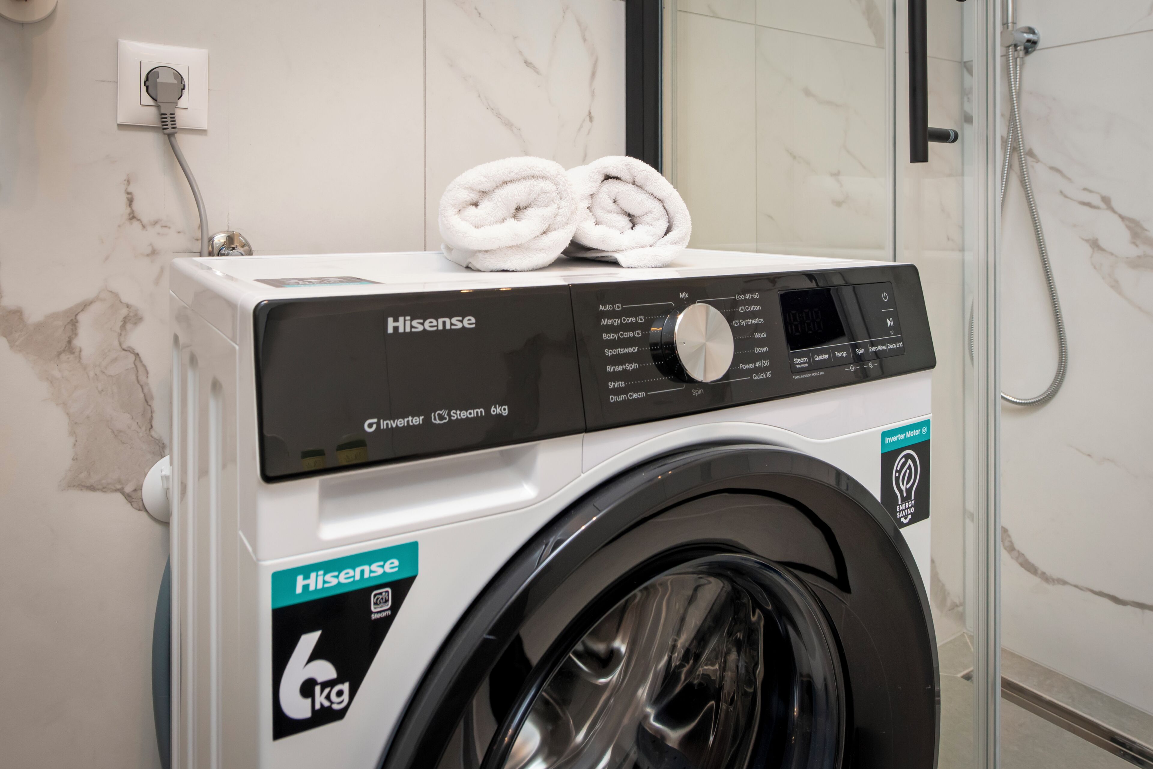 Máquina de lavar roupa Hisense de 6kg com abertura frontal, numa casa de banho com chuveiro.