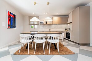 A modern kitchen with a central island, white chairs, pendant lighting, and a geometric floor pattern.