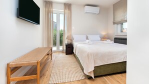Un dormitorio con cama, televisión, ventana con cortinas y aire acondicionado.