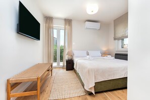 A bedroom with a bed, a TV, a window with curtains, and an air conditioning unit.