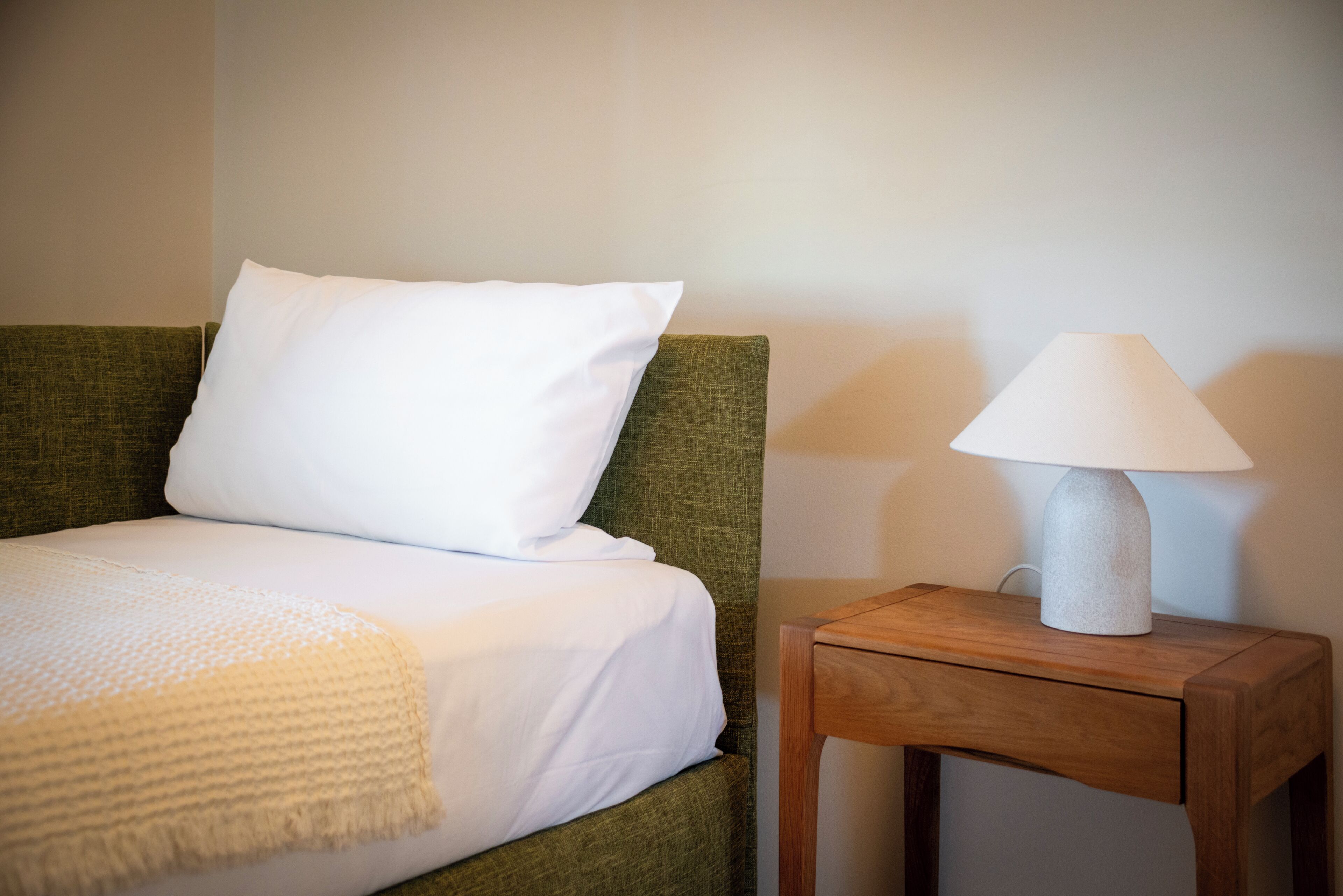 A bed with white bedding, a green headboard, and a wooden nightstand with a lamp.