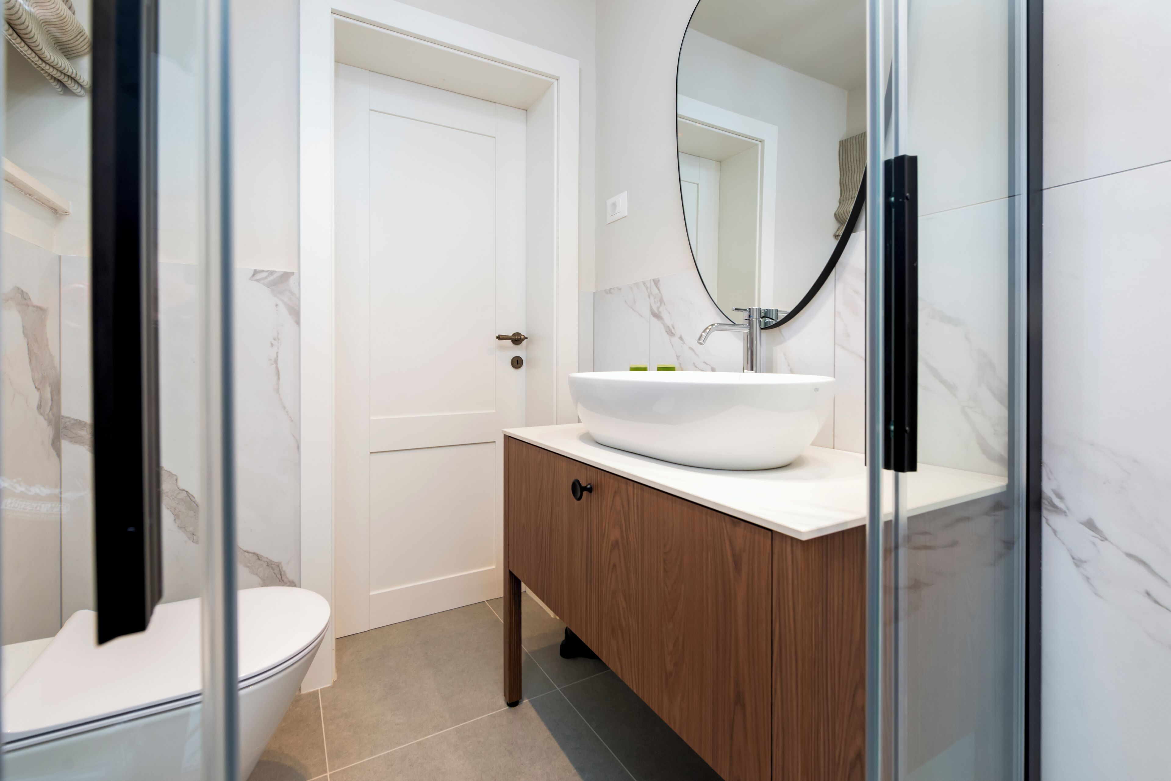 A bathroom with a white toilet, a wooden vanity with a white sink, and a large mirror.