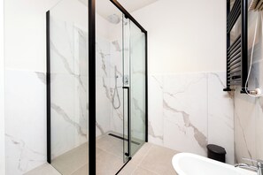 A modern bathroom with a glass-enclosed shower, a white bathtub, and marble walls.
