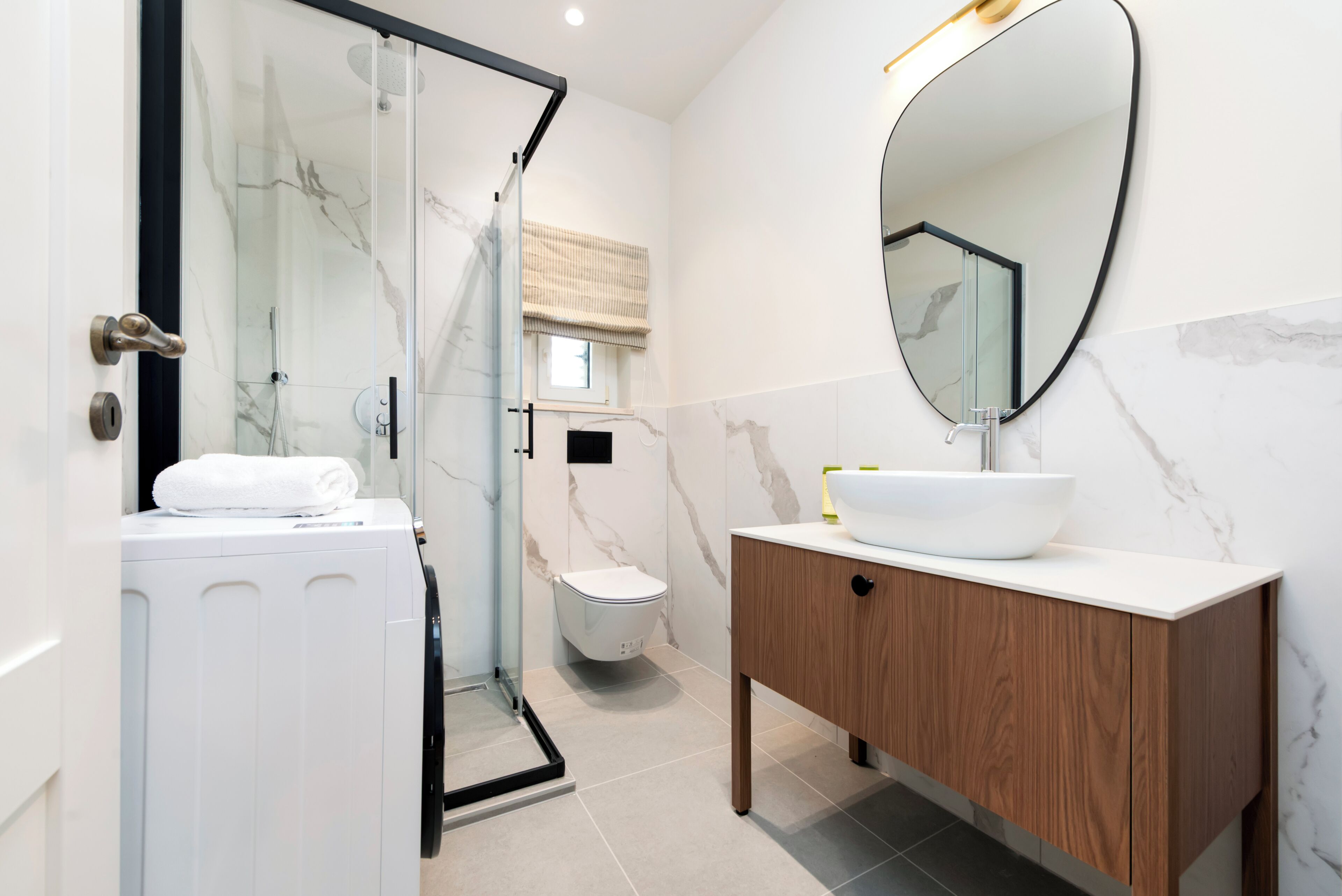 A bathroom with a glass shower enclosure, a white toilet, a wooden vanity with a white sink, and a large mirror.