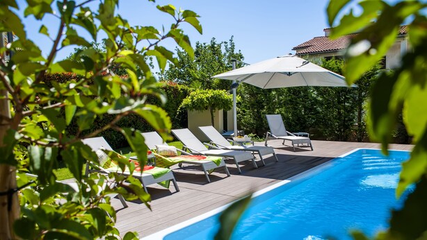 Una piscina con sillas de descanso y una sombrilla, rodeada de follaje.