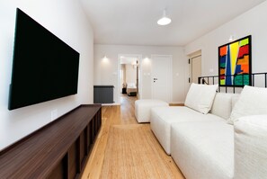 A modern living room with a flat-screen TV, a sofa, a wooden bench, and a colorful abstract painting on the wall.