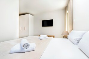 A hotel room with a bed, a TV mounted on the wall, a wooden nightstand, and a lamp.