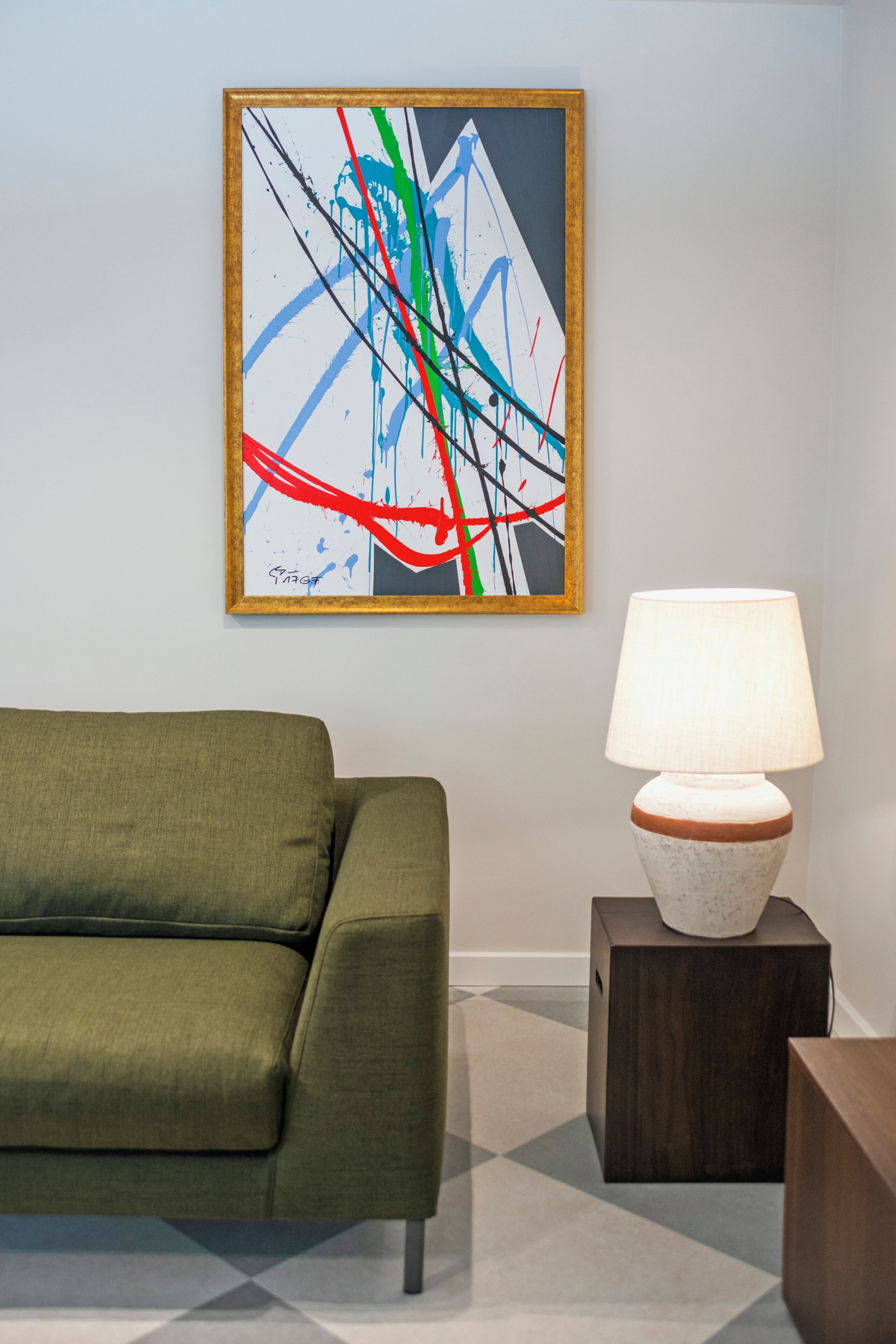 A modern living room with a green sofa, a lamp on a wooden side table, and a colorful abstract painting on the wall.