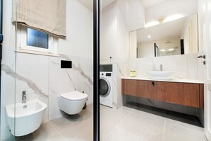 A modern bathroom with a bidet, toilet, washing machine, and a large mirror.