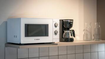 Eine Küche mit einer weißen Bosch-Mikrowelle, einer schwarzen Kaffeemaschine und zwei klaren Glasflaschen auf einem Regal.