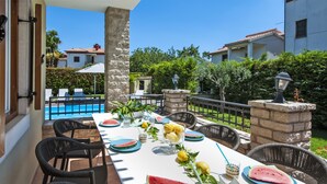 Un área de comedor al aire libre con vista a la piscina, pilares de piedra y sillas de mimbre.