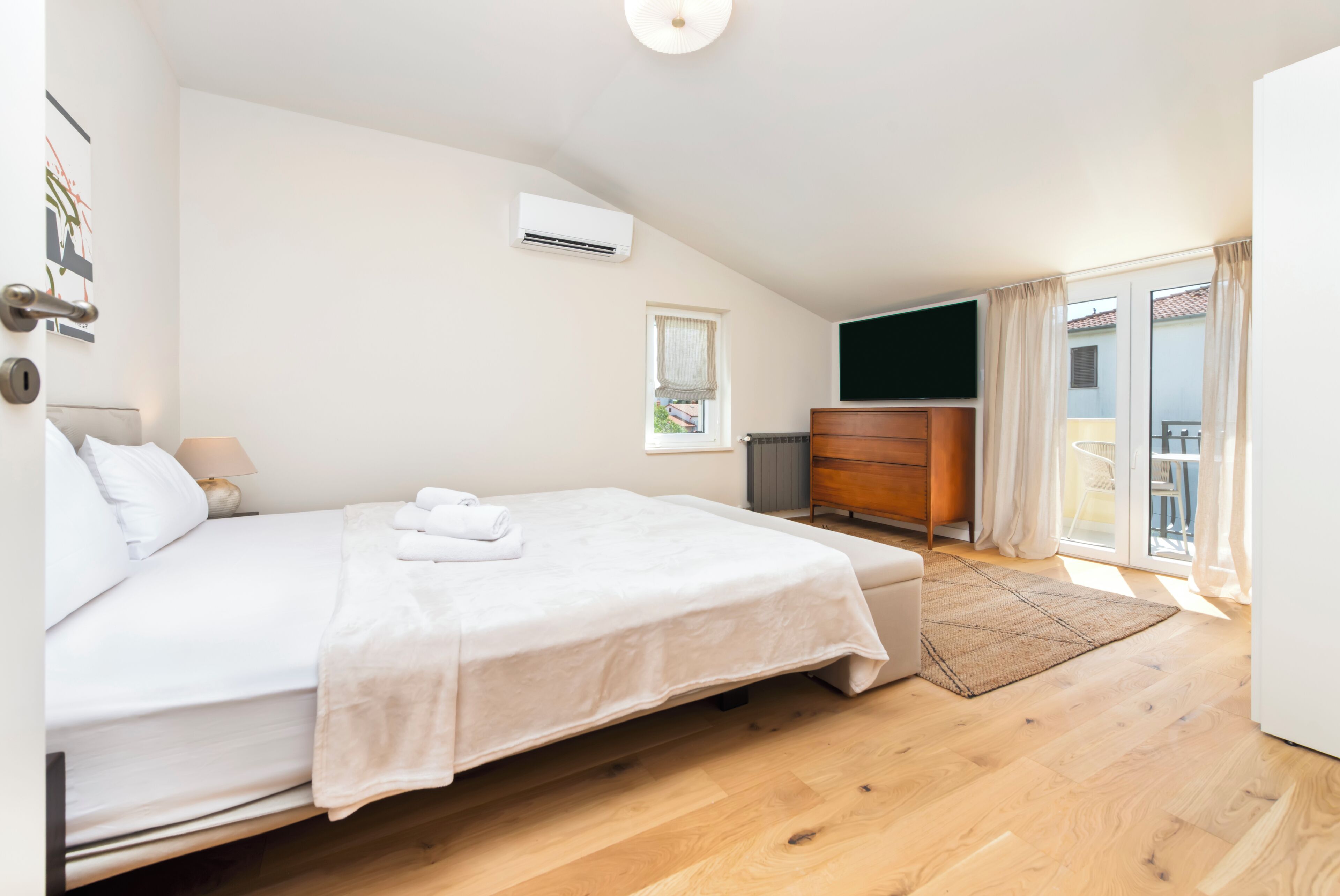 A bedroom with a bed, a dresser, a window, and a balcony.