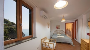 Una camera da letto con un letto, una sedia, una cassettiera e vista sul mare.