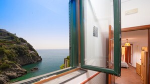 A balcony with a view of a coastal landscape, a wooden door, and a room with a bed and a dresser. - Casa di mare, Exclusive Property on the beach, private terraces, stanning views (Maiori)