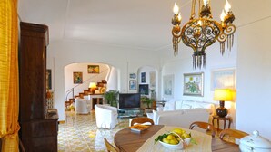 A spacious living room with a TV, white furniture, a chandelier, and artwork on the walls. - Lo sguardo sul mare, Luxury Ravello Villa, Private Pool, Great View, parking (Ravello)