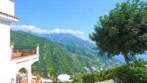 A balcony with potted plants, a white building, and a mountainous landscape in the background. - Lo sguardo sul mare, Luxury Ravello Villa, Private Pool, Great View, parking (Ravello)