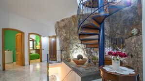 A spacious room with a stone wall, a wooden staircase, and a green door leading to another room.