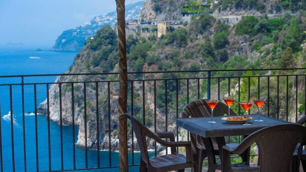 A balcony with a table set for two, overlooking a coastal cliff.