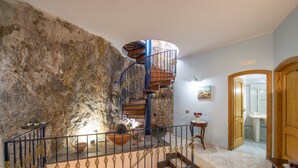 A spiral staircase with a rustic stone wall, a small table with flowers, and a wooden door.