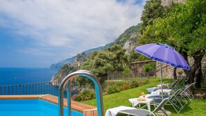 A poolside area with a view of the sea and a mountainous backdrop.