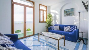 Sala de estar com sofá azul, mesa de centro e uma grande janela com vista para o verde.