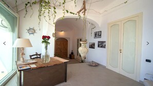 A room with a wooden desk, a vase with flowers, a hanging plant, and a door with pictures on the wall. - Villa Cindarella, Exclusive Property in Positano, private jacuzzi, near beach! (Positano)
