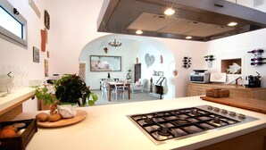 A modern kitchen with a central island, a dining area with a chandelier, and a living space visible through an archway. - Villa Cindarella, Exclusive Property in Positano, private jacuzzi, near beach! (Positano)