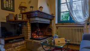 A cozy living room with a fireplace, a television, and a glass coffee table. - Noce, Characteristic chalet in Umbria with SPA, jacuzzi, garden, stunning view. (Piedicolle)