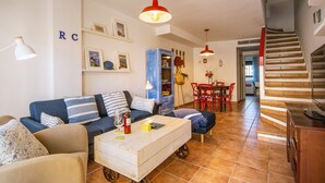 Een woonkamer met een bank, salontafel en rode hanglampen. Aan de rechterkant een trap en een eetgedeelte met rode stoelen.