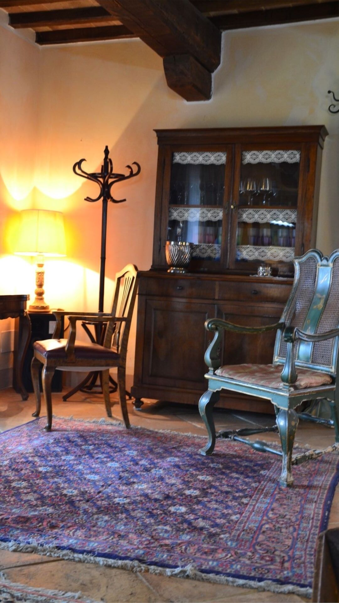 Une pièce avec un meuble en bois doté de portes en verre, un tapis à motifs et un luminaire suspendu.