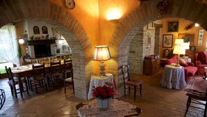 A cozy interior with stone arches, a dining area with wooden furniture, and a living room with a red armchair and a table lamp. - Al boschetto, Luxury pool Villa in Umbria, SPA, outdoor space, garden, pizzaoven (Piedicolle)