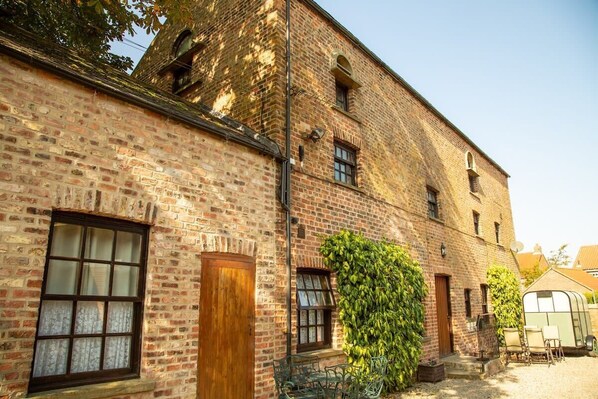 A brick building with a window, a door, and a small garden area with a bench and a greenhouse.
