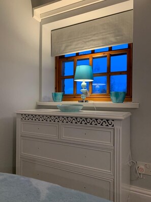 A bathroom with a window, a white vanity with drawers, a blue lamp, and two blue bowls on the windowsill.