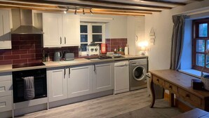 A compact kitchen with built-in appliances, a window with curtains, and a wooden table.