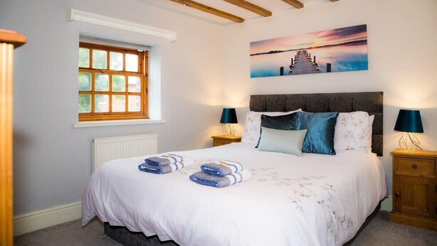 A bedroom with a bed, two bedside tables, a window, and a painting on the wall.