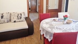 A cozy living area with a sofa, a dining table with a lace tablecloth, and a vase with flowers.