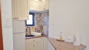 A compact kitchen with white cabinets, a wooden countertop, a sink, and a kettle.