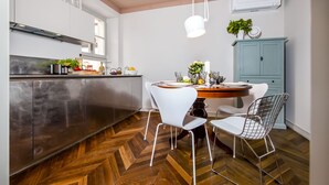 A modern kitchen with a herringbone wood floor, white chairs, and a dining table set for four. - Campitelli Design Apartment (Rovinj)
