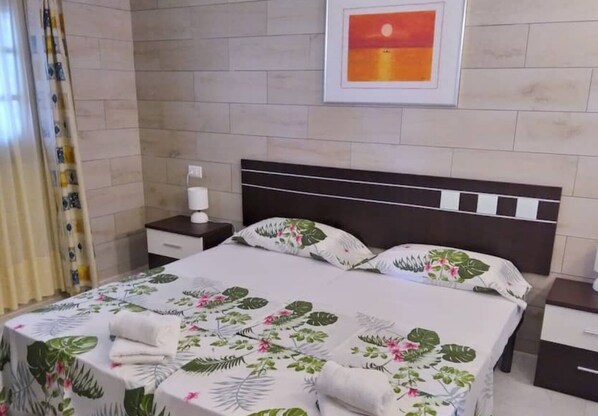 A hotel room with a bed, a nightstand, a framed picture on the wall, and a curtain.