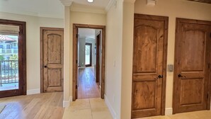 Un pasillo con puertas de madera, suelo de baldosas y vista a un balcón.