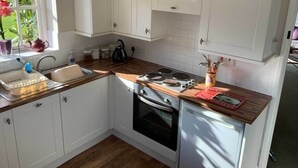 A compact kitchen with white cabinets, a wooden countertop, a stove, and an oven. - Hayloft Cottage - Devon (Sidmouth)