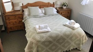 A neatly made bed with a floral-patterned bedspread, two pillows, and two folded towels on the bed. - Hayloft Cottage - Devon (Sidmouth)