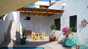 Un espace piscine doté d’une terrasse en bois, d’une table avec des chaises et de plantes en pot.