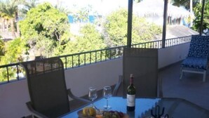 Un balcon avec une table dressée pour deux personnes, agrémentée d’une bouteille de vin, de verres et d’un assortiment de fruits.
