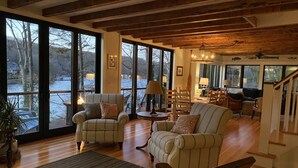 Amplia sala de estar con ventanas grandes, vigas de madera y un rincón de estar acogedor.