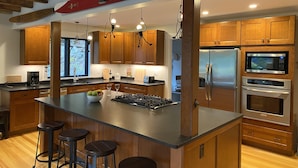 Una cocina moderna con armarios de madera, una isla central con taburetes, electrodomésticos de acero inoxidable e iluminación colgante.